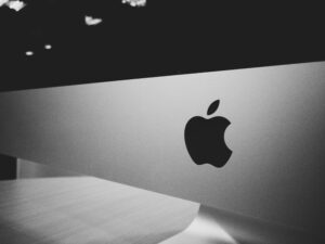 Close-up black and white photograph of an Apple iMac, featuring the Apple logo on the lower part of the screen with a sleek metallic finish. 