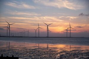 Wind turbines against a sunset sky, reflecting on the water.